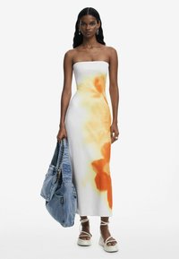 Strapless white dress with orange and yellow abstract patterns, paired with a denim bag and platform sandals with ankle straps.