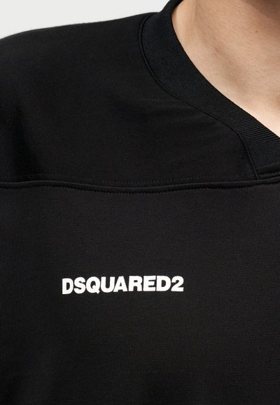 Μαύρο πουκάμισο με λευκό κείμενο "DSQUARED2" τυπωμένο στο στήθος και V-σχήμα λαιμόκοψη που φοράει ένα άτομο.