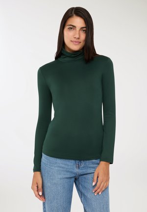 Maglione a collo alto verde a maniche lunghe realizzato in un tessuto morbido e elastico. Presenta una silhouette aderente e una leggera lucentezza. Abbinato a jeans blu chiaro.