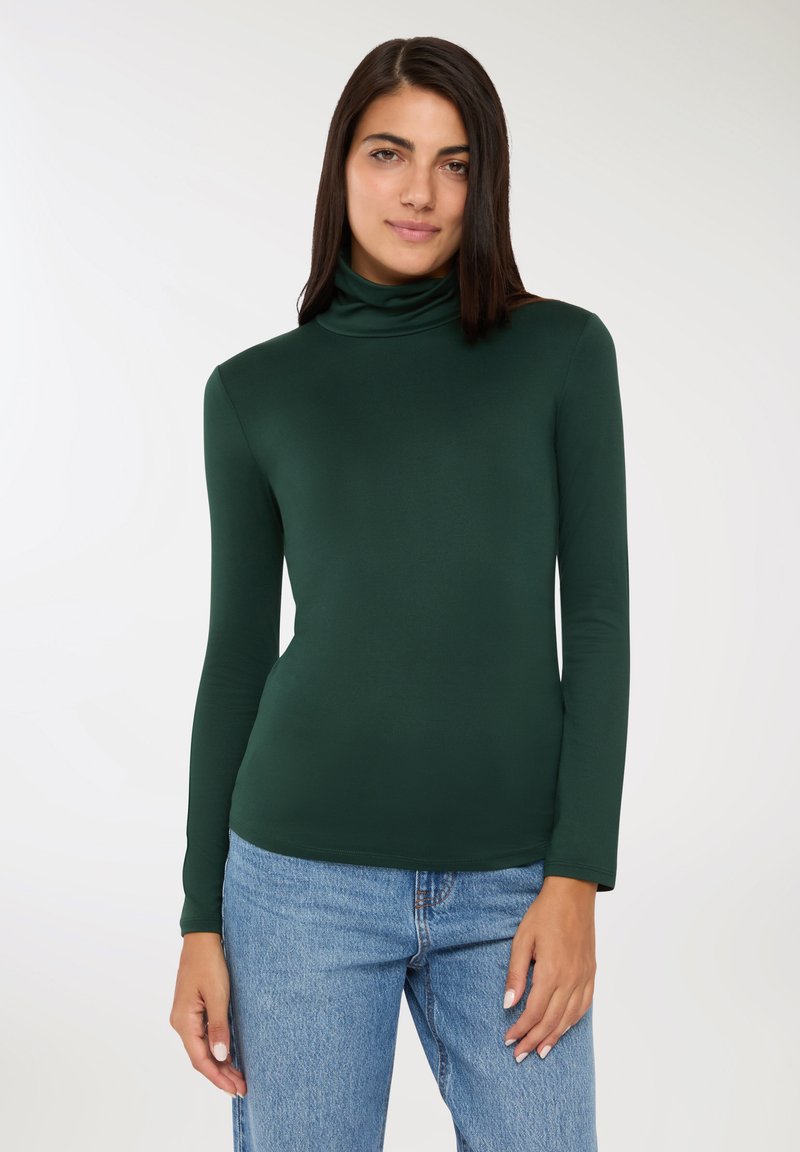 Zielony long-sleeve golf z gładkiego, elastycznego materiału. Posiada dopasowany krój i subtelny połysk. W zestawie z jasnoniebieskimi dżinsami.