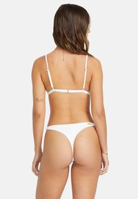 Bílý bikini s tenkými ramínky a minimalistickým designem. Materiál má jemnou texturu a kovové detaily na ramínkách a vzadu.