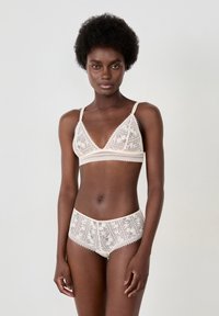 Lace bralette with a triangular shape and thin straps, paired with matching lace hipster briefs. Soft beige color with intricate floral patterns.