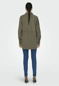Camicia a maniche lunghe verde oliva con colletto, polsini abbottonati e orlo dritto, abbinata a jeans skinny blu e tacchi.