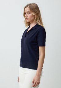 Granatowa koszulka polo z krótkim rękawem, dekoltem w serek i żebrowanymi akcentami, w zestawie z białymi spodniami. Gładki materiał o klasycznym, dopasowanym kroju.