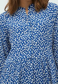 Blaues, blumengemustertes Kleid aus leichtem Stoff, mit Rundhalsausschnitt, Knopfverschluss und gerafftem Taillenbereich mit Falten.