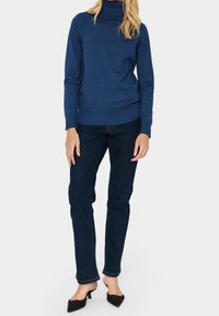 Niebieski sweter z golfem wykonany z miękkiego materiału, zestawiony z ciemnymi dżinsami i czarnymi butami na obcasie, zaprezentowany na jednolitym tle.