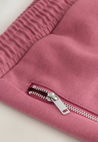 Primo piano di tessuto rosa con una cintura elastica e una cerniera argentata parzialmente aperta su una tasca.