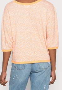 Light orange shirt with a textured pattern of small white and blue dots, featuring a wide neckline and three-quarter sleeves.