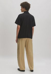 Zwarte short-sleeve shirt met een kraag, gecombineerd met relaxte beige cargo pants met meerdere zakken. Glad stoftextuur.