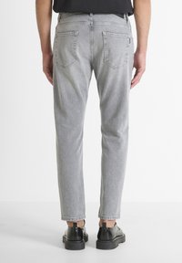 Vaqueros de mezclilla gris con un diseño de pierna recta, que cuentan con dos bolsillos traseros y una textura desgastada. Llevados con zapatos de vestir negros.