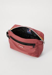 Kompakt rózsaszín nylon táska fekete cipzárral, logóval ellátott patch-csel és kontrasztos bélésével, amelyben egy cipzáras rekesz található.