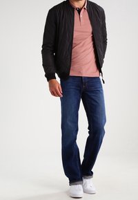 Gepatchte schwarze Bomberjacke, pinkes Poloshirt, blaue Jeans und weiße Sneakers. Einfaches Design mit gerippten Bündchen und Kragen. Glatte Texturen.