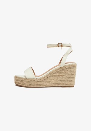 Sandały na koturnie z beżowym płóciennym cholewkiem i paskiem wokół kostki, wyposażone w plecioną podeszwę z juty i teksturowaną gumową podeszwę zapewniającą przyczepność.