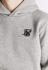 Grau Hoodie aus weichem Stoff, ausgestattet mit einem gestickten schwarzen Logo auf der linken Brustseite. Das Design umfasst eine klassische Kapuze mit Kordelzug.