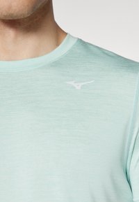 Camiseta deportiva de color verde menta claro con mangas cortas. Presenta una textura sutil y un logo blanco en el área del pecho izquierdo. Cuello redondeado.