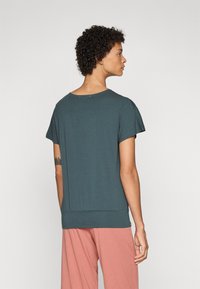 Teal relaxed-fit top with short sleeves, round neckline, and a subtly gathered waistband, paired with light pink loose-fit pants.