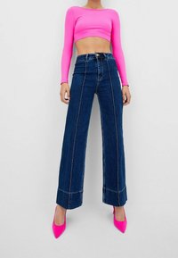 Top de manga larga ajustado en rosa brillante, combinado con unos vaqueros de pierna ancha de corte alto en denim oscuro, con costuras en contraste y amplios puños.