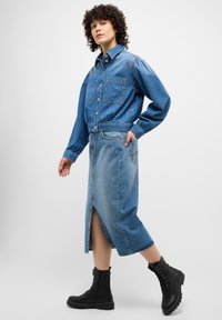 Jeansjacka med två framfickor, kombinerad med en midilång jeanskirt med en framklippt insats. Svarta snörstövlar fulländar looken.