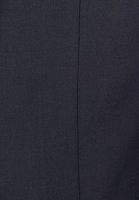 Zbliżenie ciemnej tkaniny z pionowym szwem biegnącym przez środek.