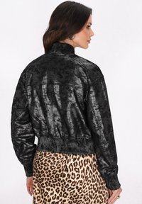 Jachetă bomber din piele ecologică neagră, cu un finisaj texturat, tiv elastic și mansete. Pur tată peste o fustă cu imprimeu leopard.