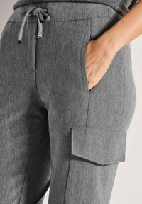 Persoon in een grijze broek met een elastische tailleband en cargozakken, met een hand in een van de voorzakken.