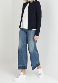 Námořnický žebrovaný cardigan s otevřeným předním designem; bílá košile pod ním. Světle modré široké džíny s třepeným lemem. Bílé tenisky dokončují outfit.