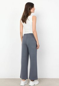 Volné šedé široké kalhoty s elastickým pasem, kombinované s bílým bezrukávovým topem. Bílé tenisky celý outfit doplňují.