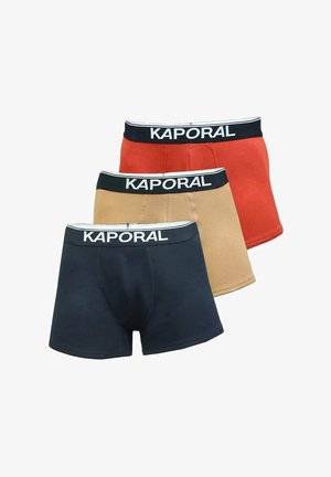 Trois paires de boxers pour hommes en bleu marine, beige et rouge. Chacune a une ceinture noire avec "KAPORAL" imprimé en blanc. Matière en coton doux.