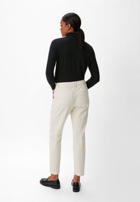 Schwarzer Rollkragenpullover mit glatter Textur, kombiniert mit cremefarbenen, maßgeschneiderten Hosen und schwarzen Slippern. Rückansicht.