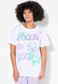 Hvid bomulds T-shirt med farverigt graffiti-lignende tekst i pink, grøn og lilla, samt former som hjerter og stjerner. Korte ærmer.
