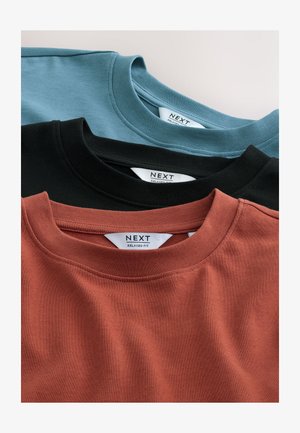 Kolm lõdva lõikega ümmarguse kaelusega T-särki: türkiissinise, musta ja roostepunase tooniga, millel on sile puuvillane tekstuur ja õmmeldud kaelused. Valged sildid on nähtavad.