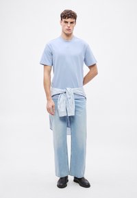 Világoskék, kerek nyakú póló, bő szabású, világoskék farmerral párosítva. Csíkos ing megkötve a deréknál, fekete cipővel stílusosan viselve.