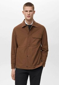 Brown lightweight jacket with a collar, front pocket, and snap buttons. Smooth texture and tailored fit, paired with a black undershirt.