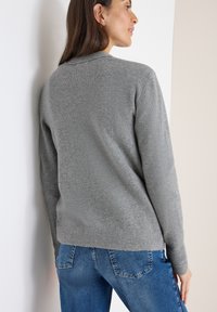 Maglione grigio a maglia con scollatura rotonda e polsini a costine, abbinato a jeans blu. Tessuto morbido e design semplice, senza motivi visibili.