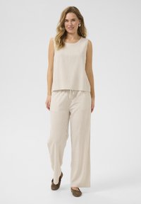 Top senza maniche a righe beige abbinato a pantaloni larghi a righe beige, entrambi in tessuto leggero, con vita regolabile e vestibilità comoda.