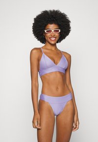 Conjunto de bikini lilás claro com parte de cima em triângulo com alças finas e parte de baixo com uma faixa larga. O tecido tem uma textura riscada subtil.