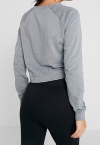 Felpa grigia cropped con maniche raglan lunghe, texture morbida e scollo rotondo, abbinata a leggings neri.