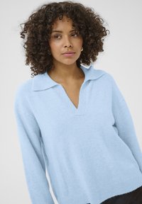 Pull-over bleu clair en tissu tricoté doux, avec un col en V et des manches longues à la coupe décontractée.
