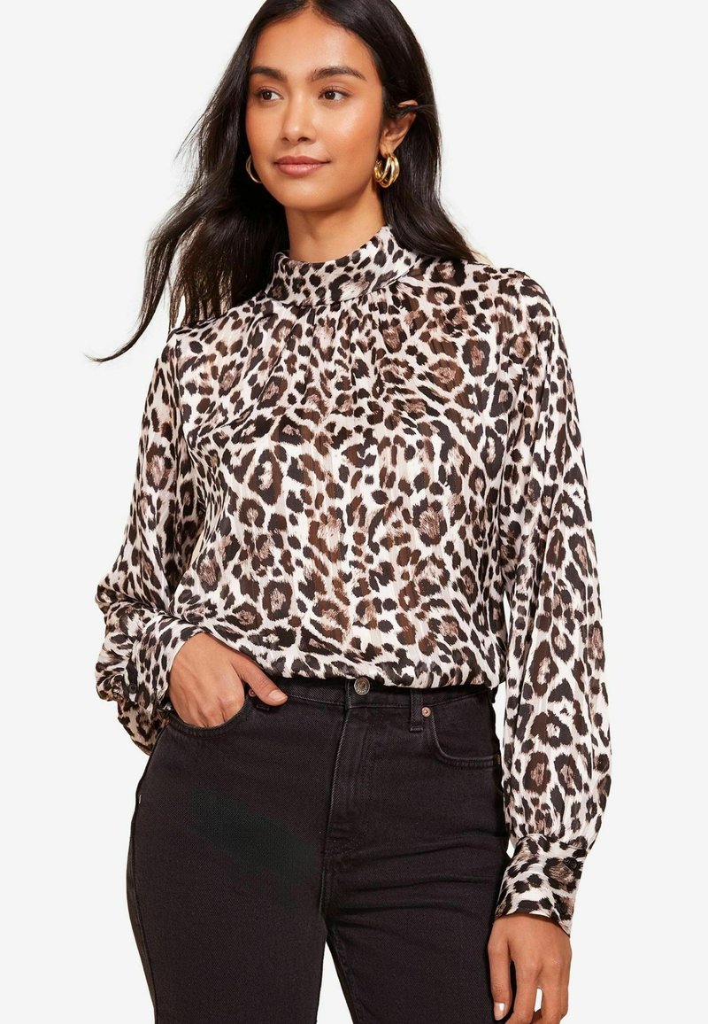 Leopardenmuster-Bluse aus glattem Stoff mit hohem Kragen, langen Ärmeln und Raffung an den Schultern. Kombiniert mit schwarzen Jeans.
