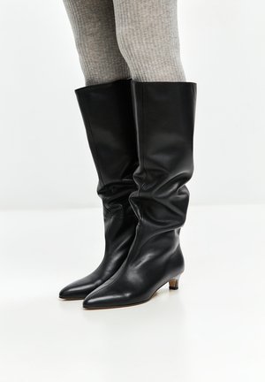 Black leather knee-high boots with a slouchy design, pointed toe, and a low heel. Smooth texture and minimalistic style.