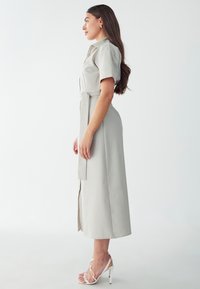 Light grey, mid-length dress with short sleeves, belted waist, and a front slit. Paired with white strappy high-heeled sandals.