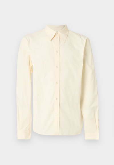 Koszula z długim rękawem z miękkiej, jasnopomarańczowej bawełny. Posiada zakończony grotem kołnierzyk, zapięcie na guziki z przodu oraz subtelny haft na piersi.