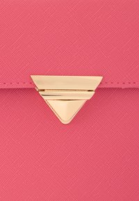 Pochette rose texturée avec un détail de fermeture triangulaire en or. Le matériau présente un léger grain, mettant en valeur une teinte vibrante.