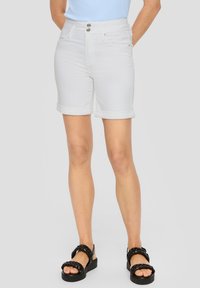 Białe dżinsowe szorty z podwiniętymi nogawkami, dopasowany krój, dwa guziki z przodu oraz dwie kieszenie. W zestawieniu z czarnymi plecionymi sandałami.