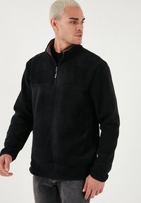 Pullover in pile nero con collo a mezza zip, texture liscia e pannello superiore a contrasto. Maniche lunghe con vestibilità rilassata.