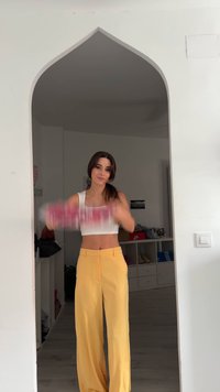 Weißes Crop-Top und gelbe weit geschnittene Hosen mit Taschen. Der Hintergrund zeigt einen hellen Raum mit Regalen und Turnschuhen.