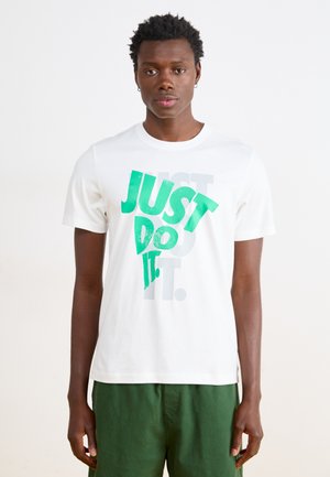 Hvid bomulds T-shirt med et grønt grafisk tekstdesign "JUST DO IT" med en struktureret finish. Parret med grønne shorts.