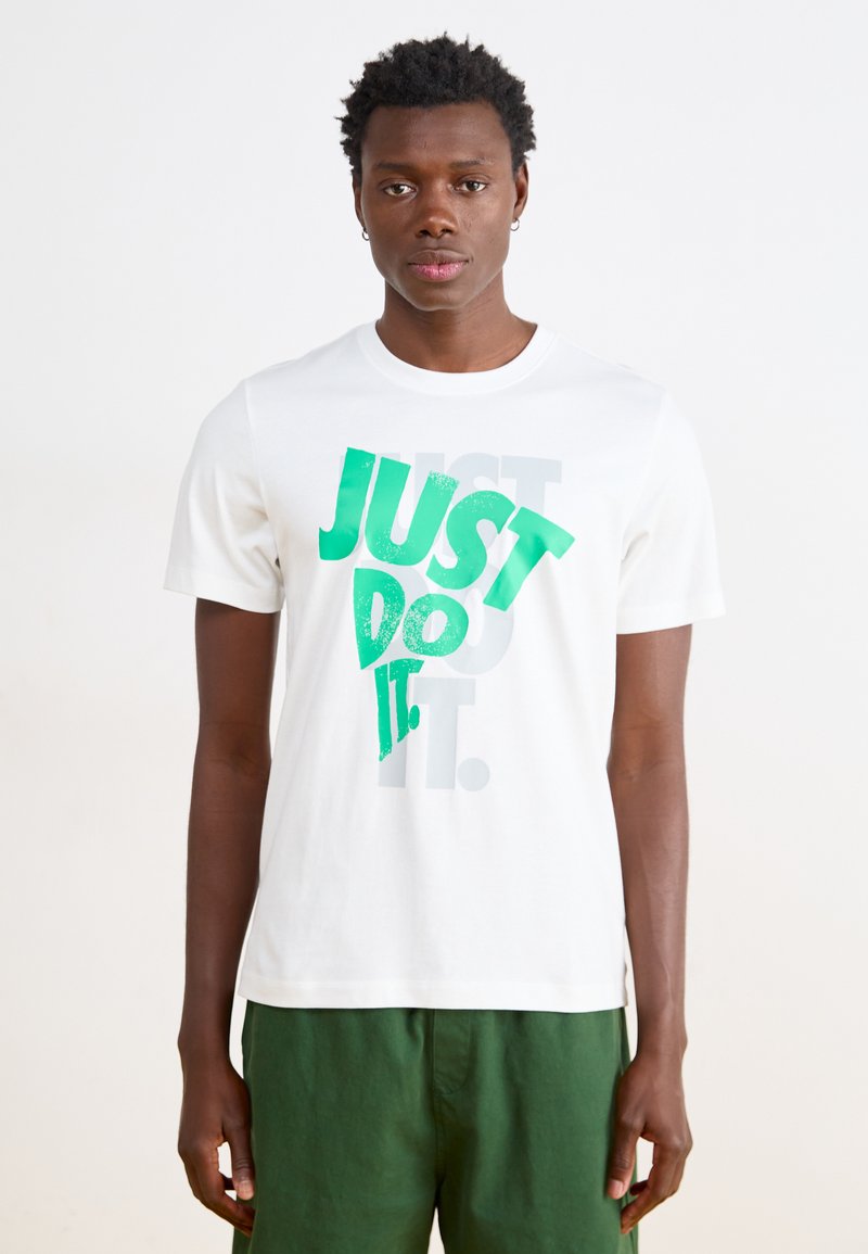 Hvid bomulds T-shirt med et grønt grafisk tekstdesign "JUST DO IT" med en struktureret finish. Parret med grønne shorts.