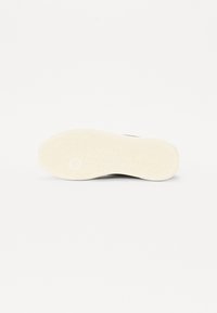 Semelle de sneaker blanche en caoutchouc avec un motif de bande de roulement texturé, présentant un design circulaire en relief et des transitions lisses dans le matériau.