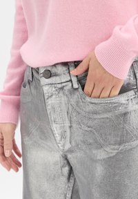 Pull en tricot rose avec des poignets côtelés associé à un jean en denim argenté brillant avec une poche frontale et une fermeture à bouton.